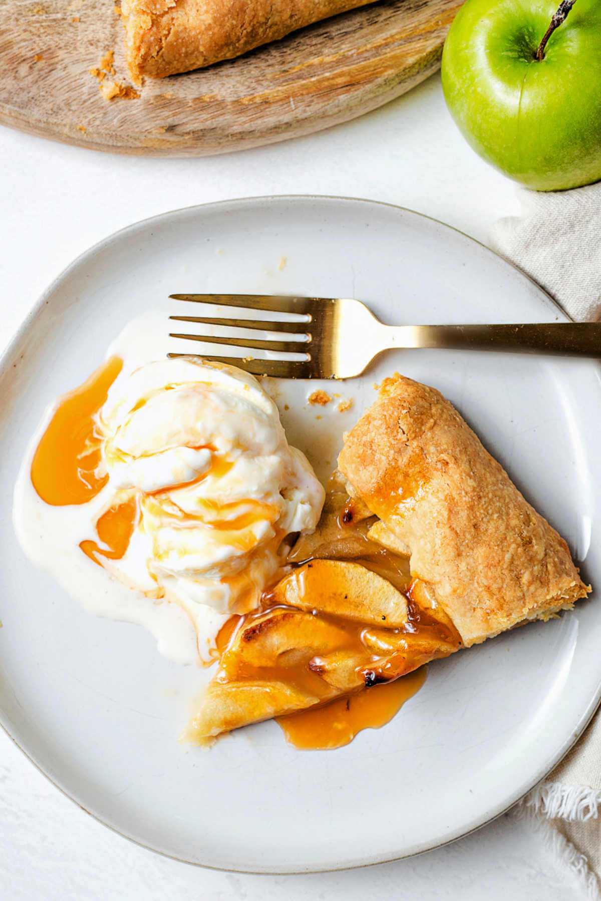 a slice of rustic apple tart on a plate with ice cream and caramel syrup.
