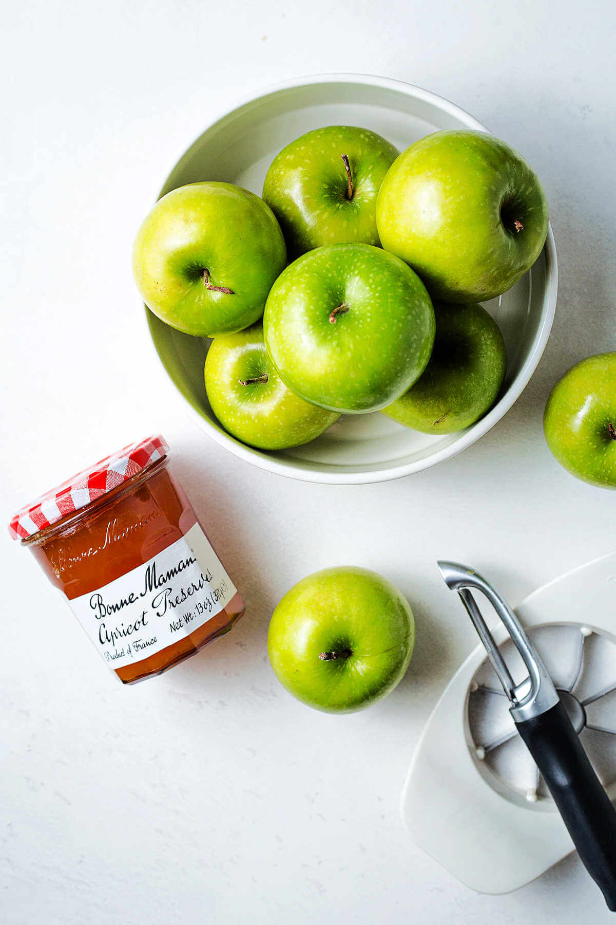 a bowl of Granny Smith apples and a jar of apricot jam on a table.