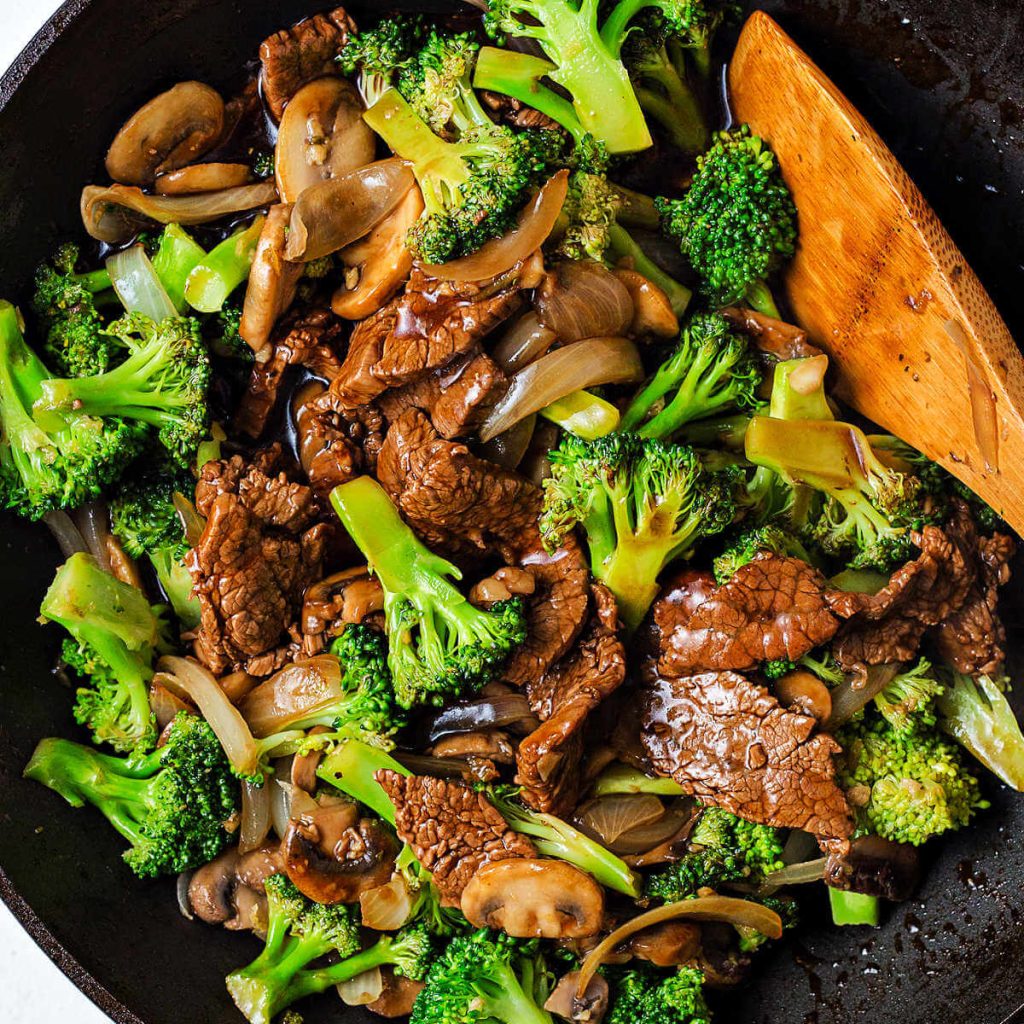 beef and broccoli in a wok with a wooden spatula.
