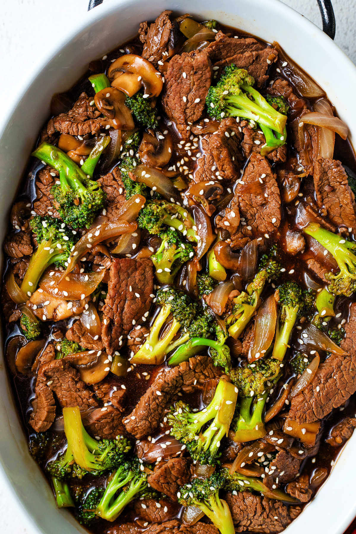 beef and broccoli in a platter garnished with sesame seeds on a table.