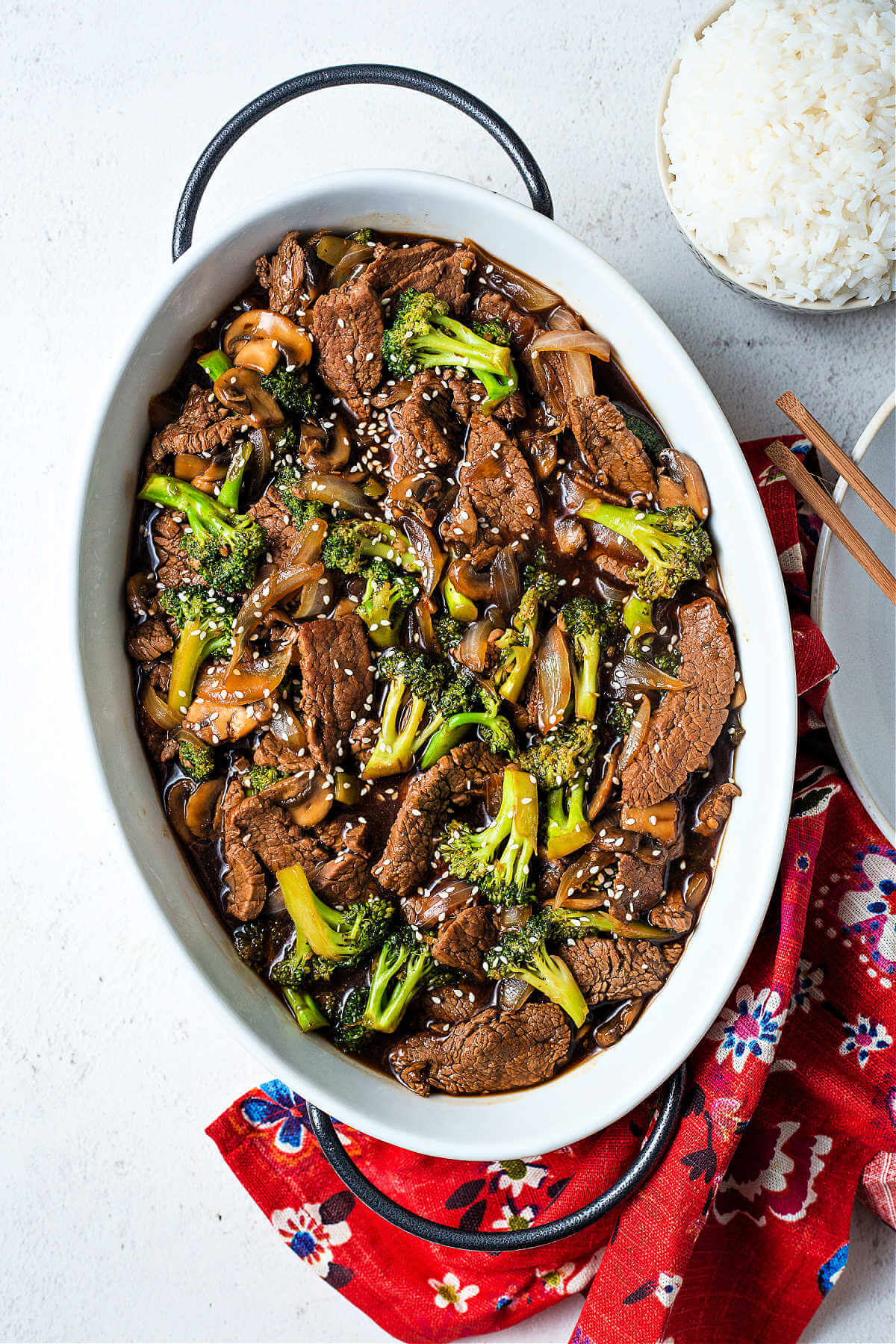beef and broccoli in a platter with a bowl of rice on a table.