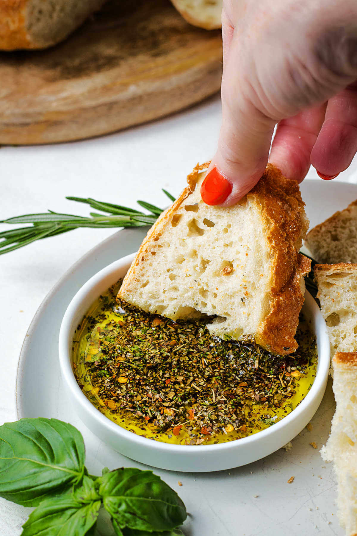 dipping a slice of bread into a bowl of olive oil dip on a table.