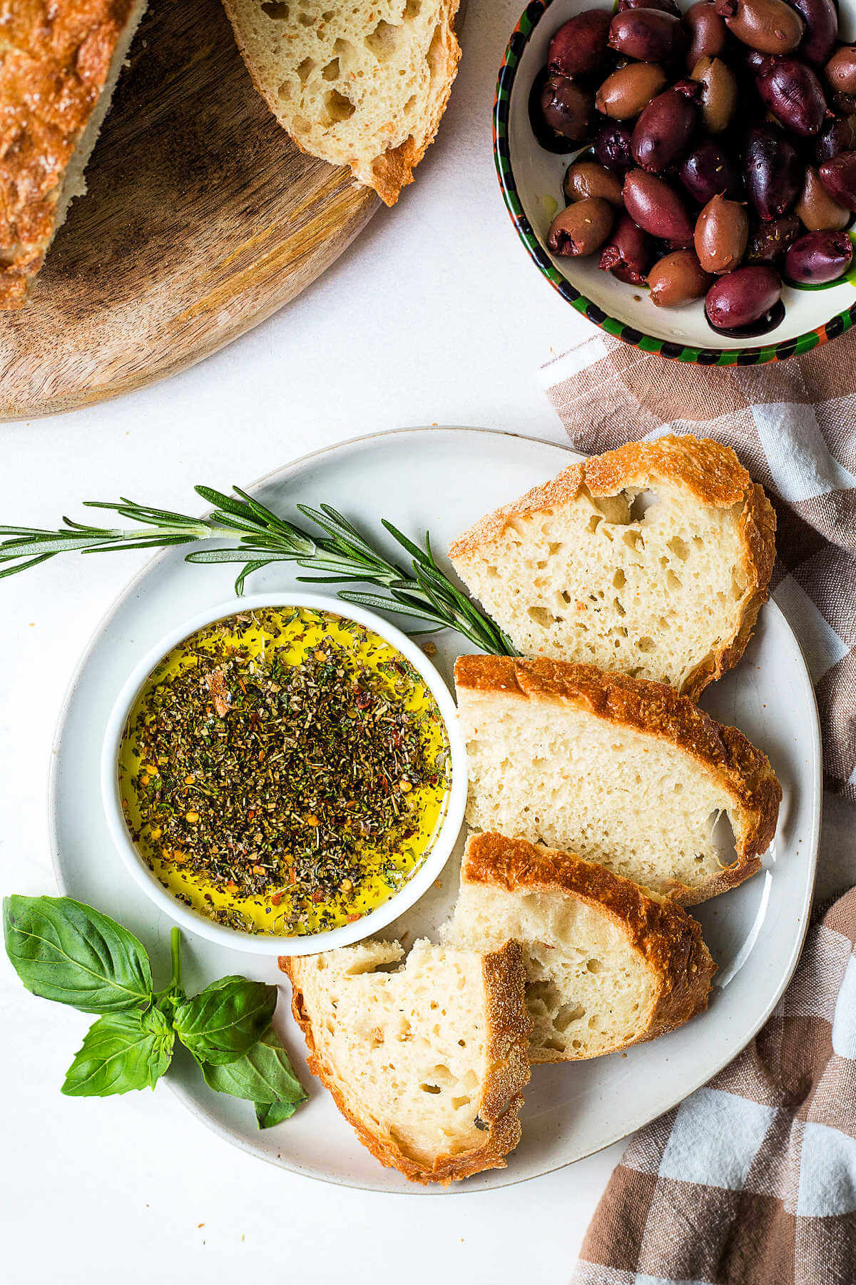 Olive Oil Bread Dip in a shallow bowl on a plate with sliced bread and a bowl of olives on a table.