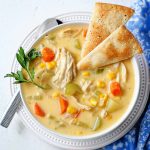 Chicken pot pie soup with pie crust crackers in a white bowl garnished with parsley on a table.