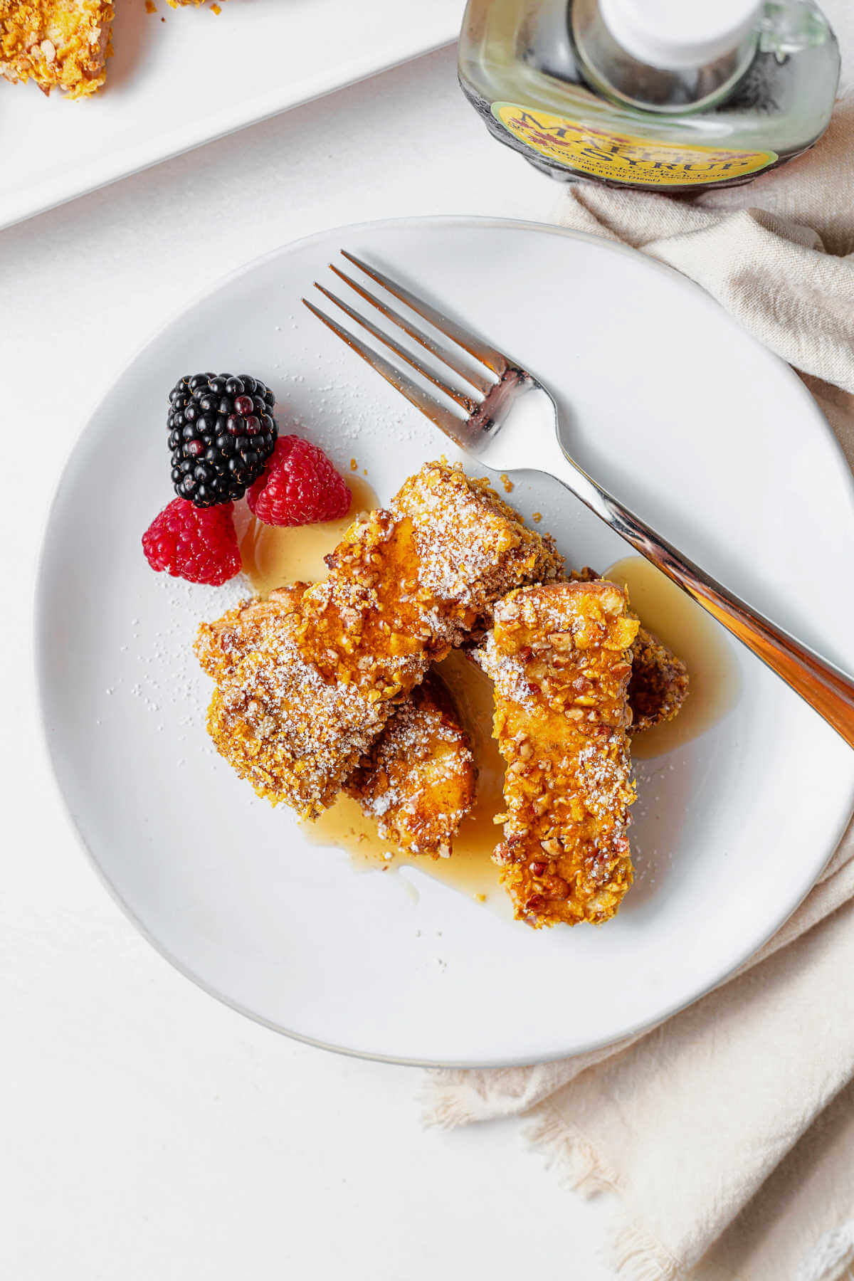 cornflake crusted French toast sticks stacked on a plate with syrup drizzled on top.