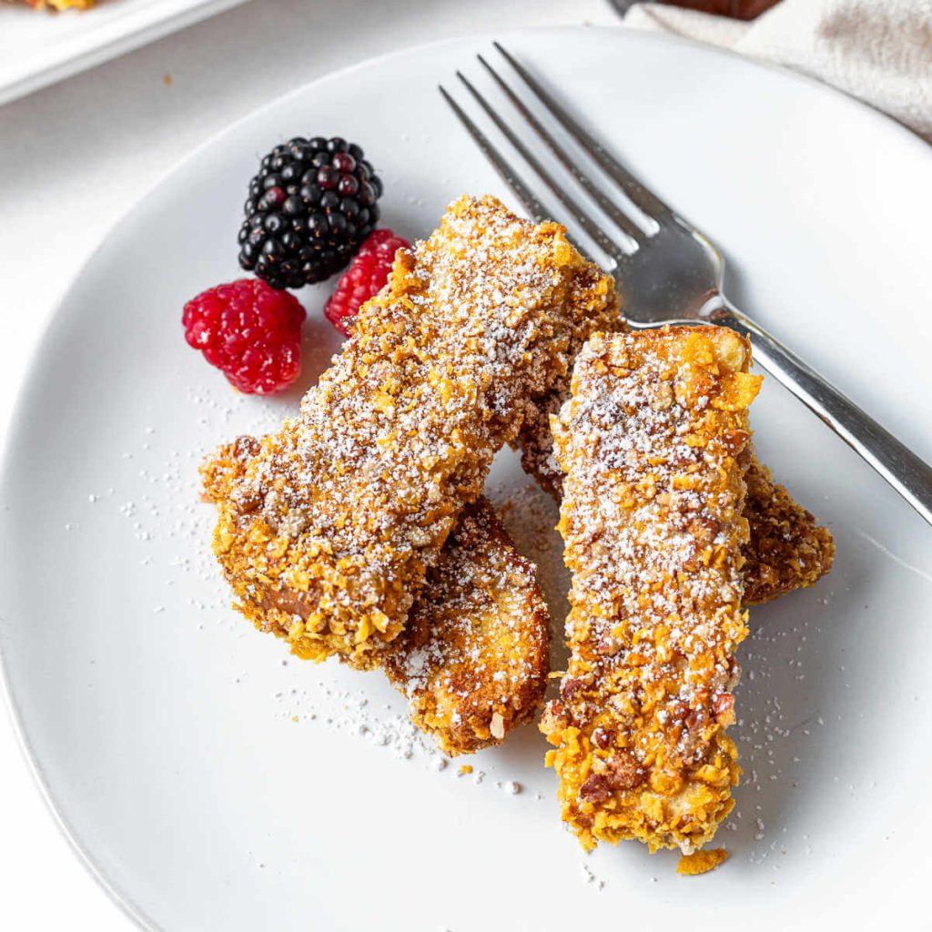 cornflake crusted French toast sticks stacked on a plate with a fork.