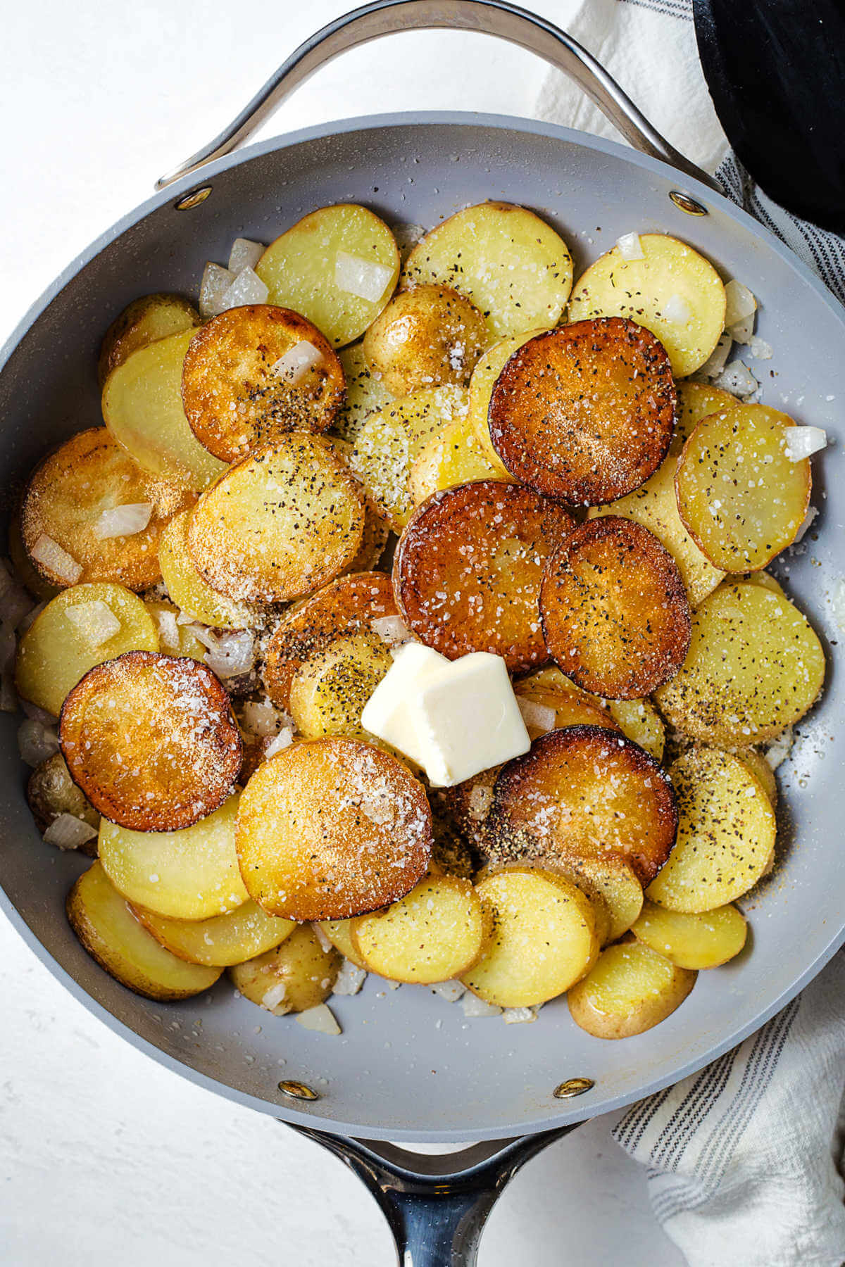 frying sliced potatoes in a skillet with spices and butter.