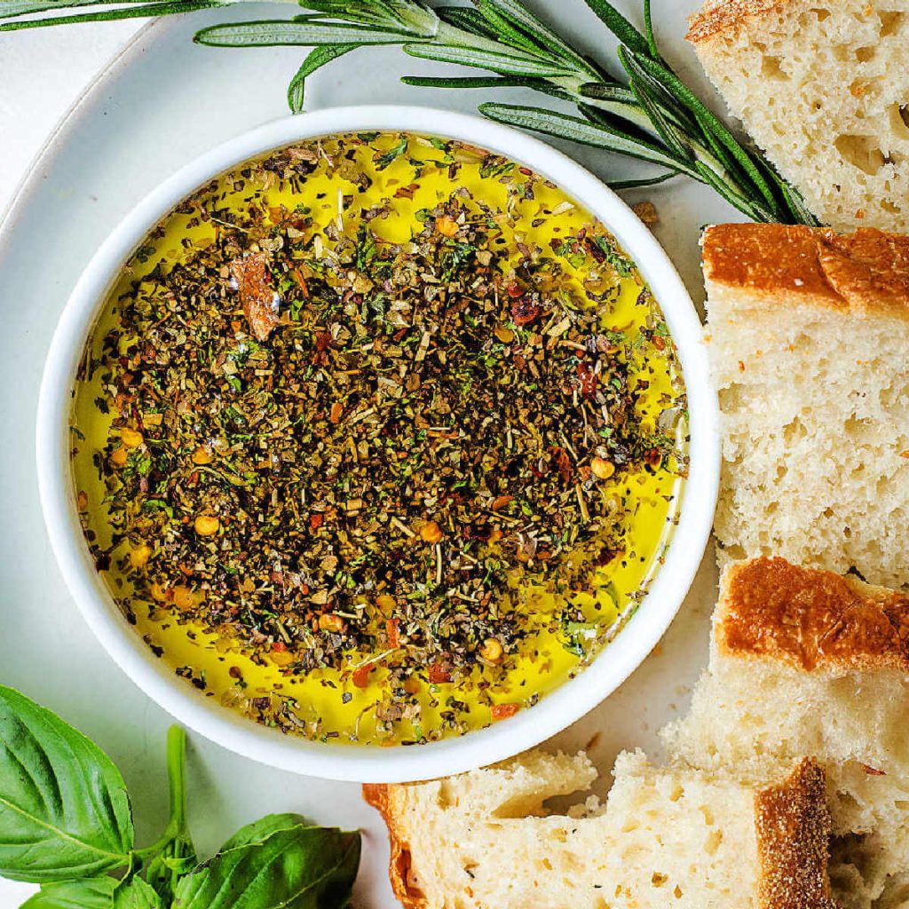 Olive Oil Bread Dip in a shallow bowl on a plate with sliced bread.