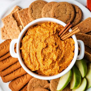 pumpkin dip in a bowl on top of a serving tray with cookies andn apple slices for serving.