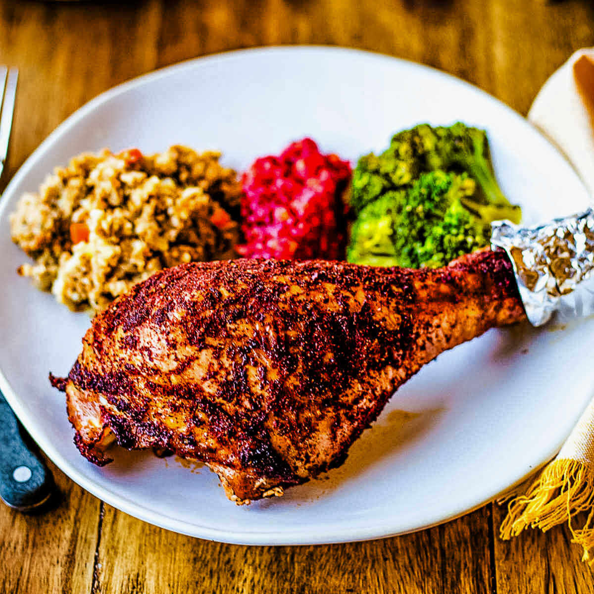 a roasted turkey leg on a white plate with sides on a wooden table