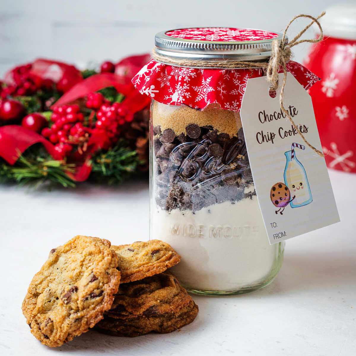 a jar of chocolate chip cookie mix on a table with a stack of cookies to the side.