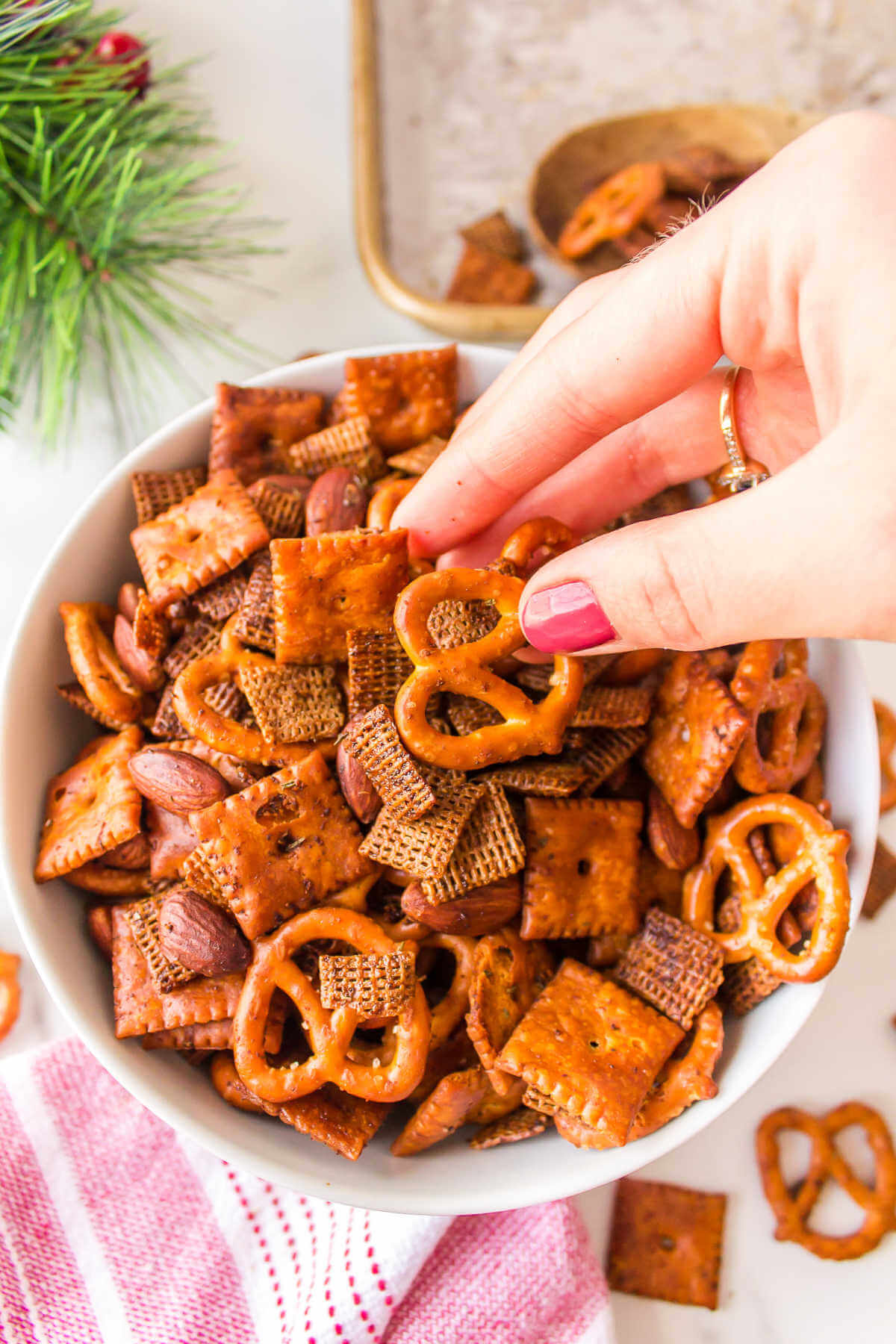a hand grabbing a bite of Chex mix from a bowl.