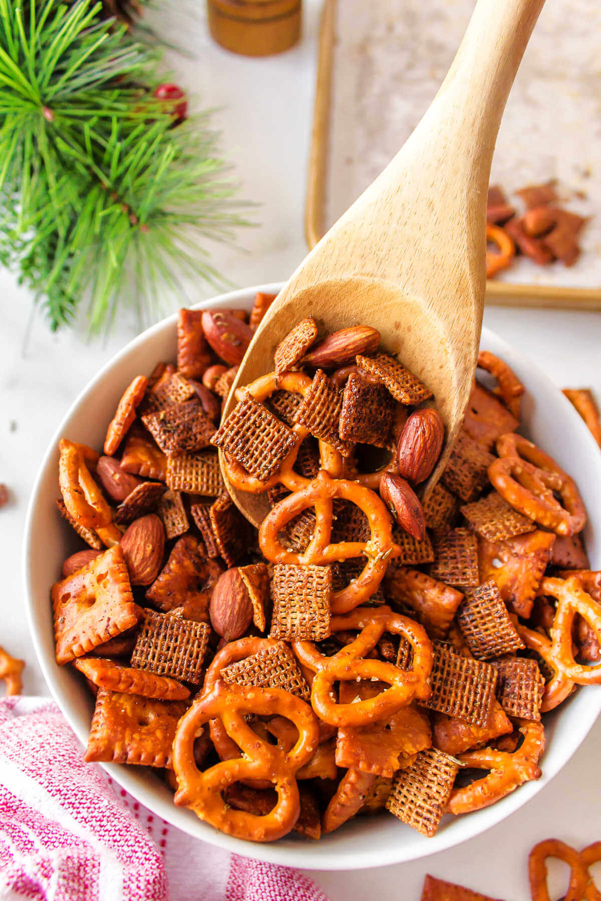 spooning Chex Mix into a serving bowl with a wooden spoon.