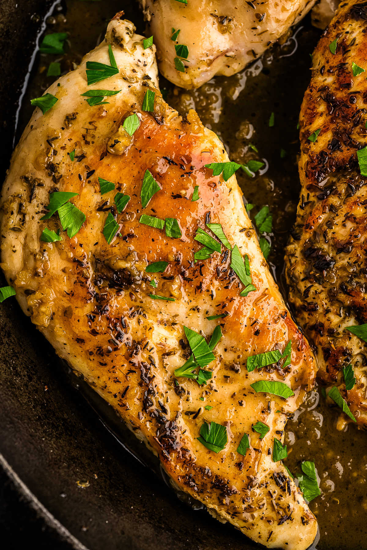 close up image of a garlic butter chicken breast in a cast iron skillet.