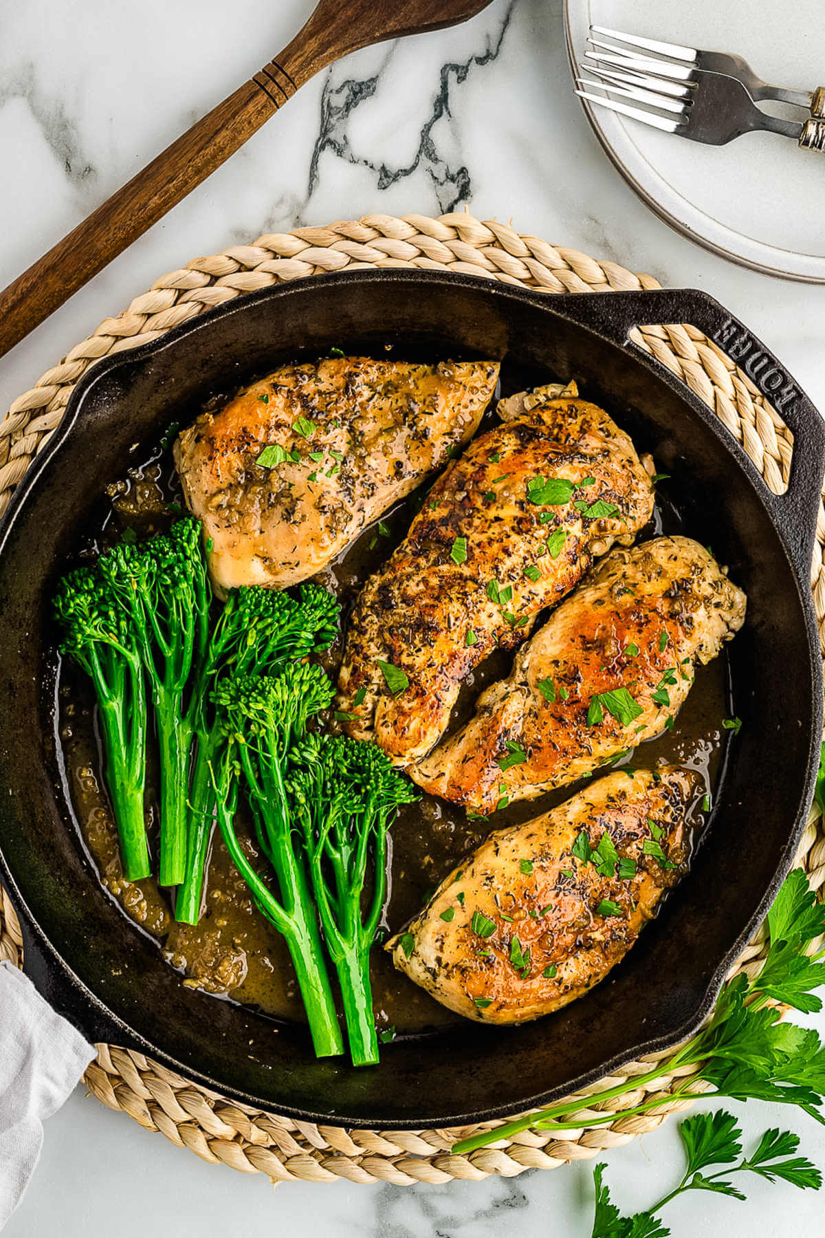 chicken in a skillet with broccolini on a table.