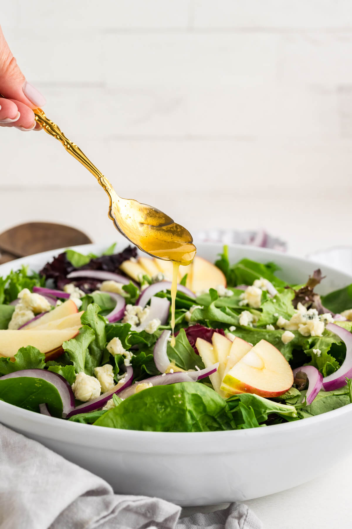 drizzling maple dijon vinaigrette over a salad in a bowl on a table.