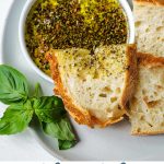 OLIVE OIL BREAD DIP ON A SERVING PLATTER WITH BREAD SLICES.