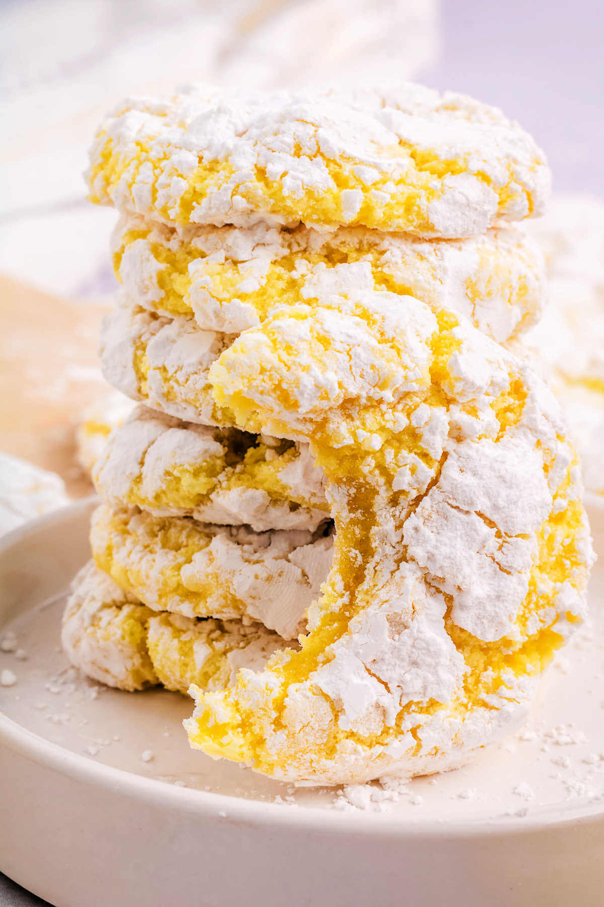 lemon crinkle cookies stacked on top of each other in a white dish on a table.