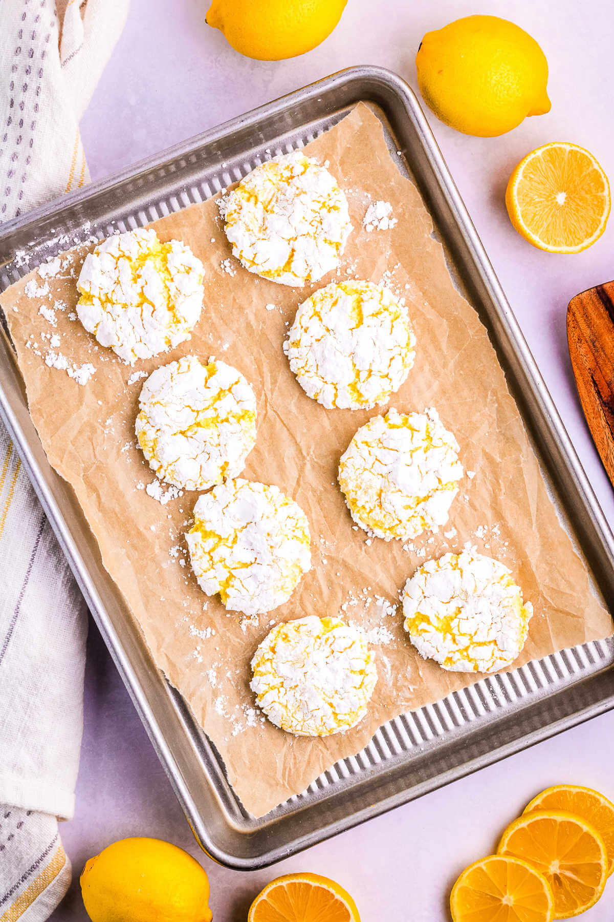 baked lemon crinkle cookies on a baking sheet on a table with lemons.