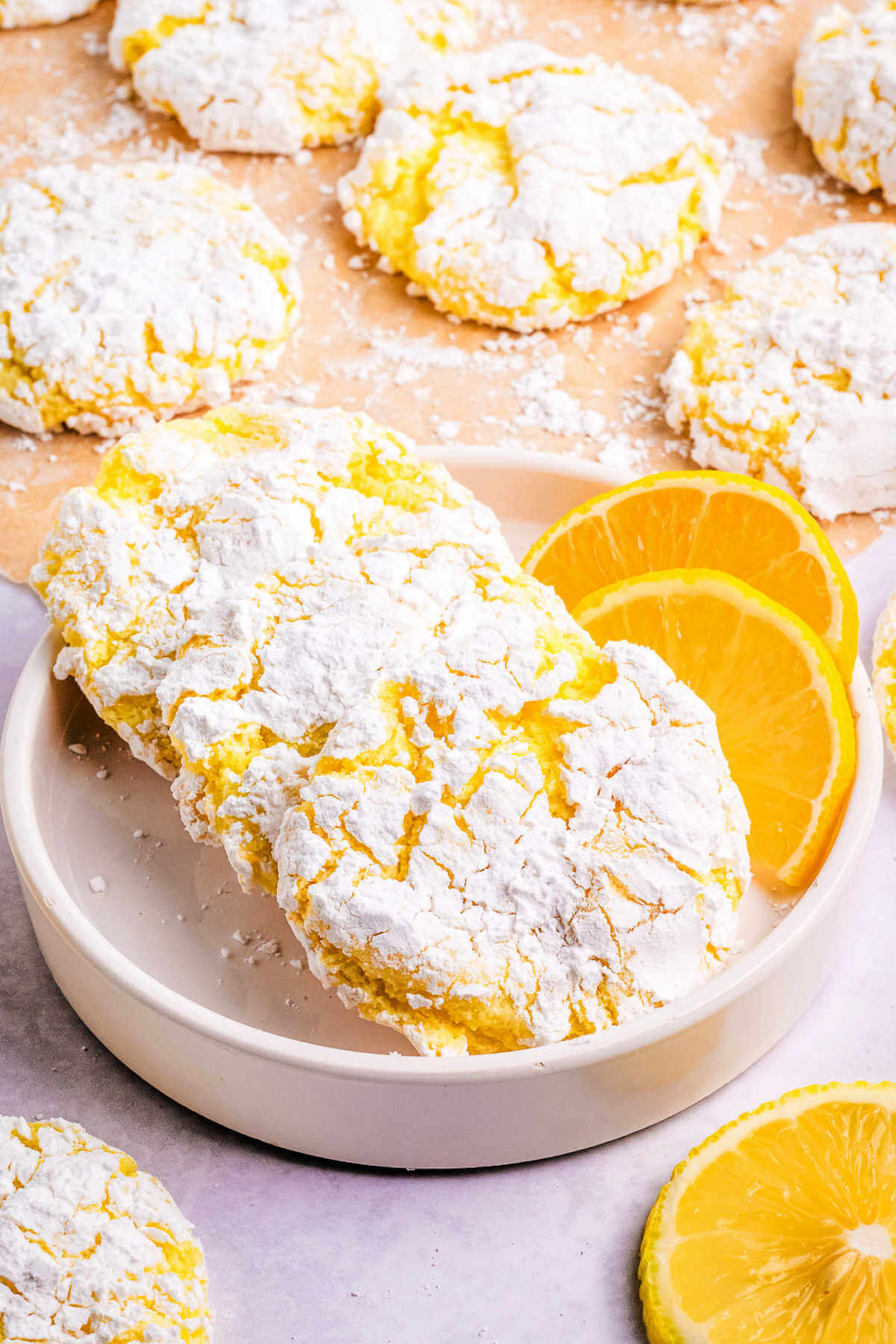 lemon crinkle cookies in a white dish with lemon slices on a table.
