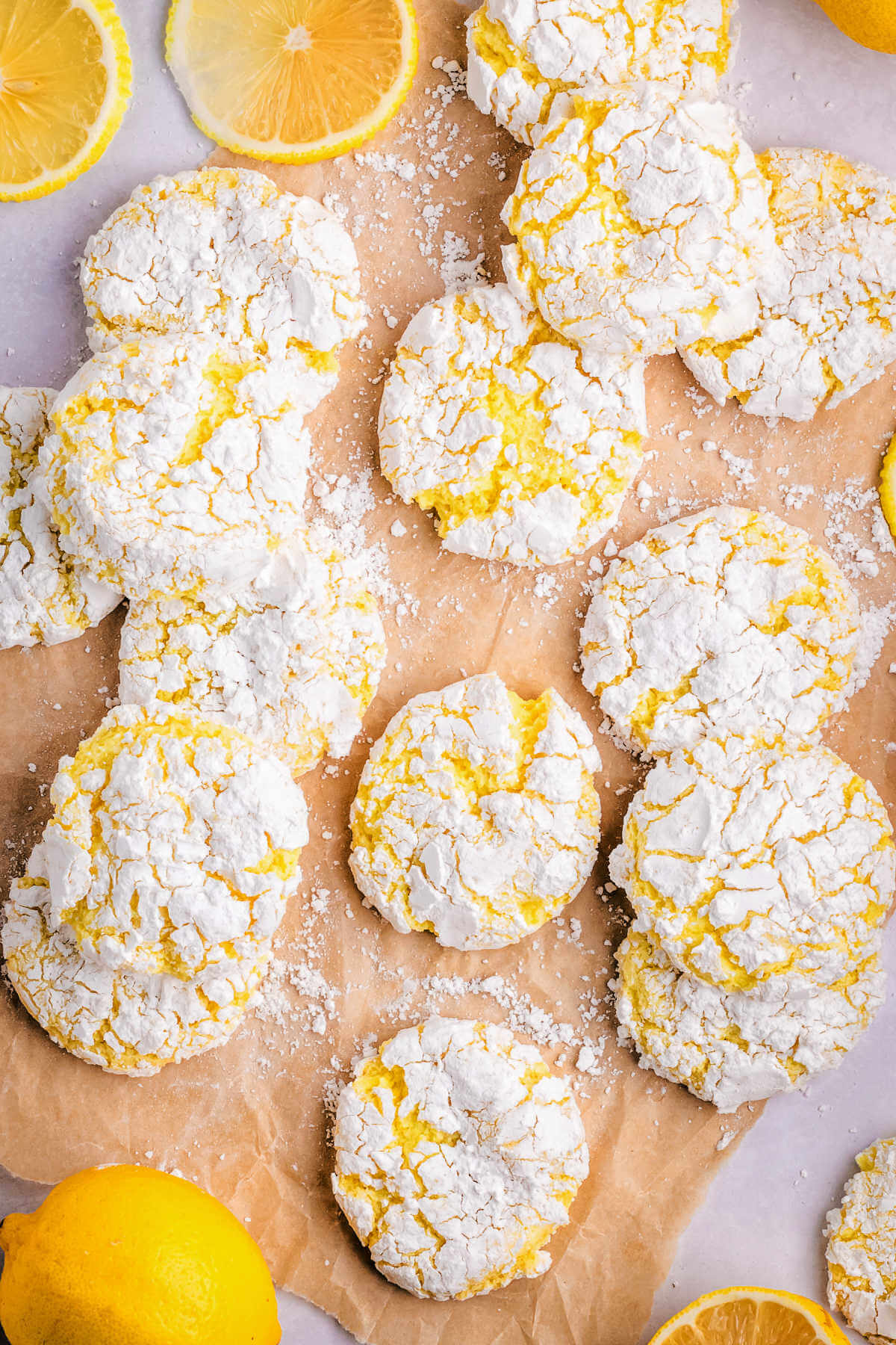 lemon crinkle cookies on parchment paper with lemon slices.