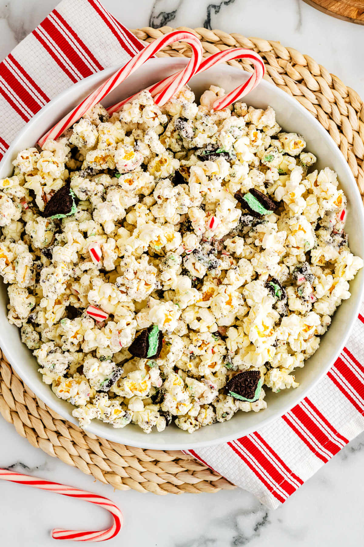 A bowl of white chocolate popcorn with peppermint and oreos on a table with candy canes.