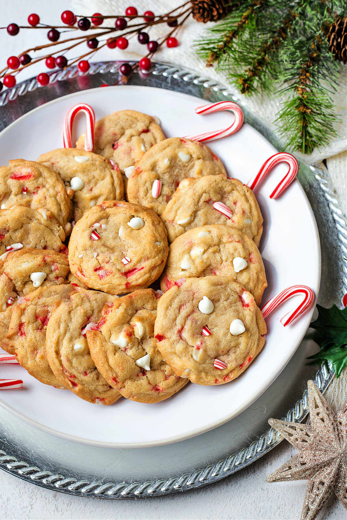 white chocolate chip peppermint cookies on a plate with candy canes on a table decorated with holiday decor.