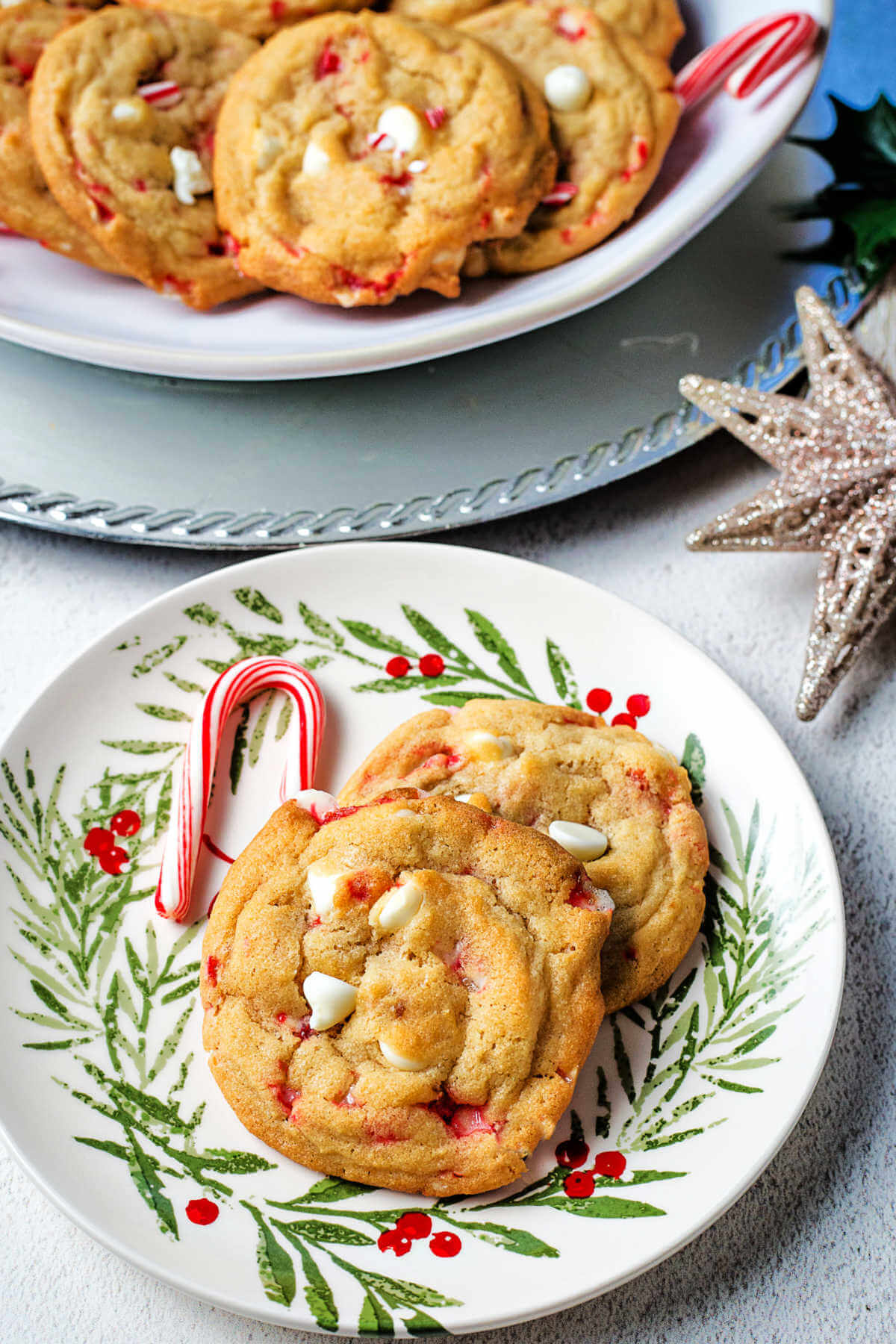 Two white chocolate chip peppermint cookies on a serving plate with candy canes on a table.