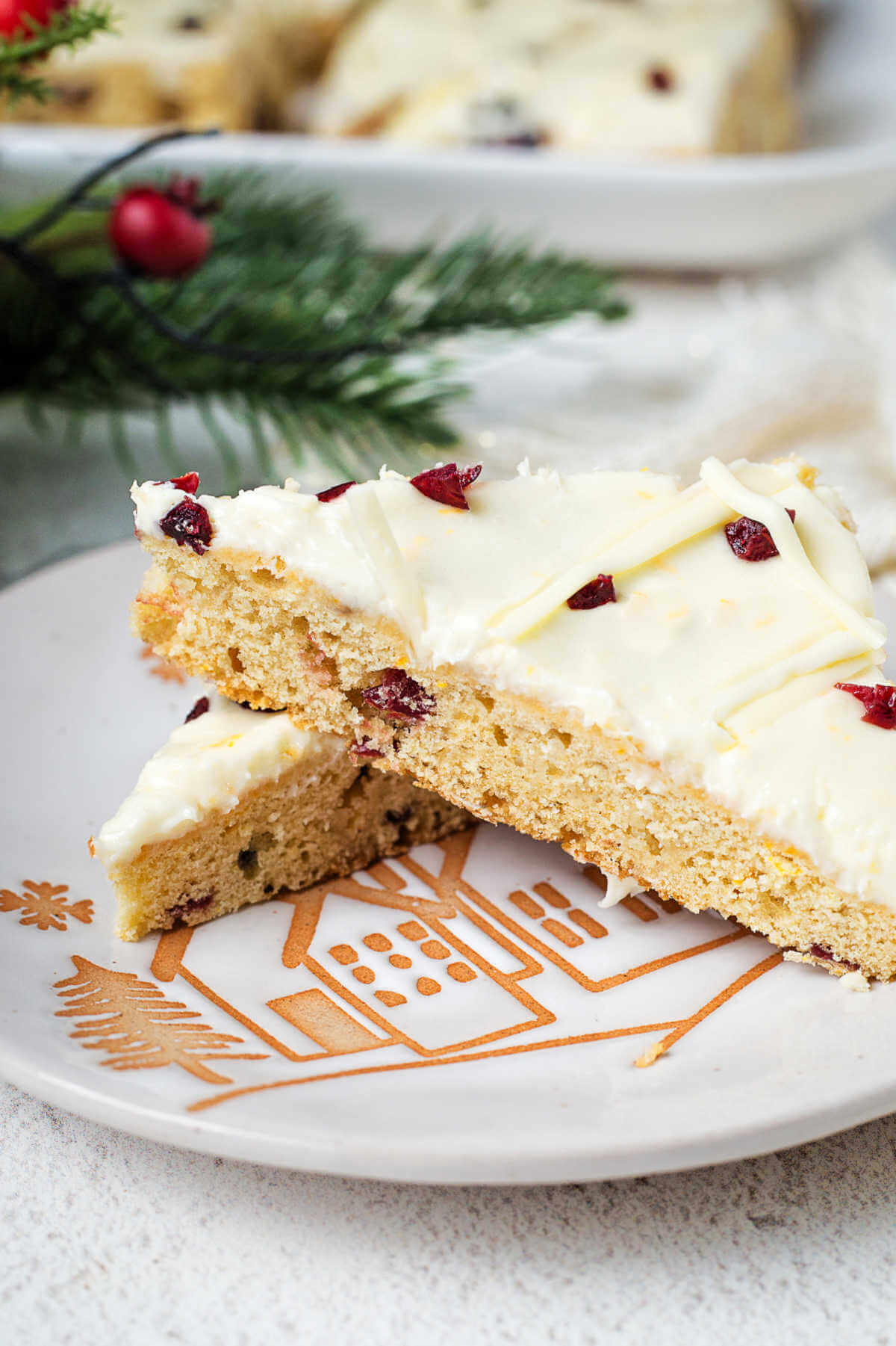 two cranberry bliss bars on a holiday serving plate on a table with Christmas decor.