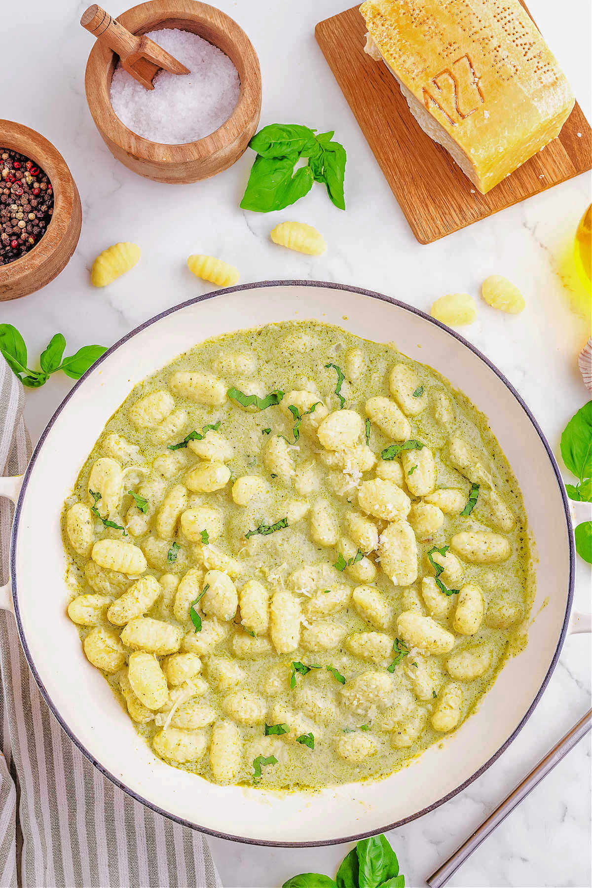 gnocchi in pesto sauce on a table with parmesan cheese and basil leaves in the background.