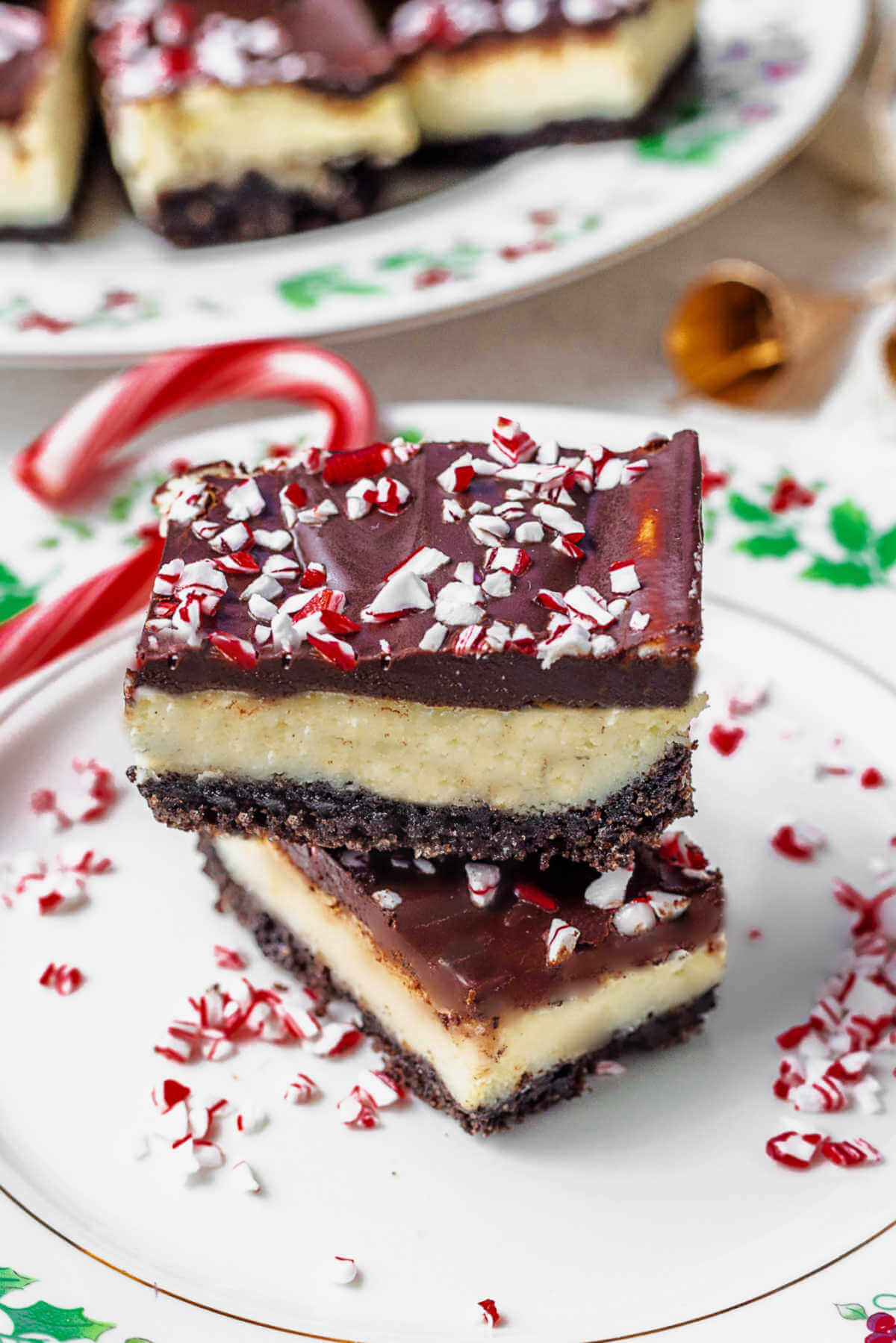 two peppermiint cheesecake bars on a china plate with candy cane bits with a plate of cheesecake bars in the background.