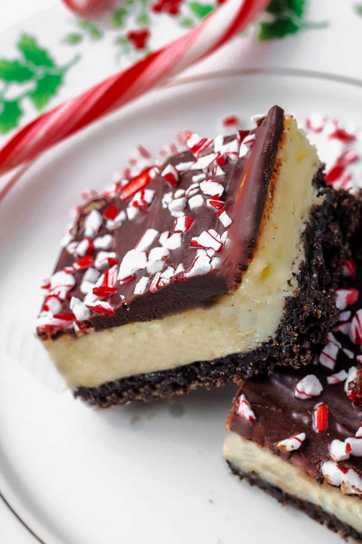 two peppermint cheesecake brownies on a plate with a candy cane.