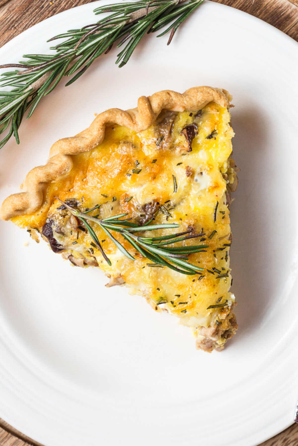 a slice of sausage quiche with a rosemary garnish.