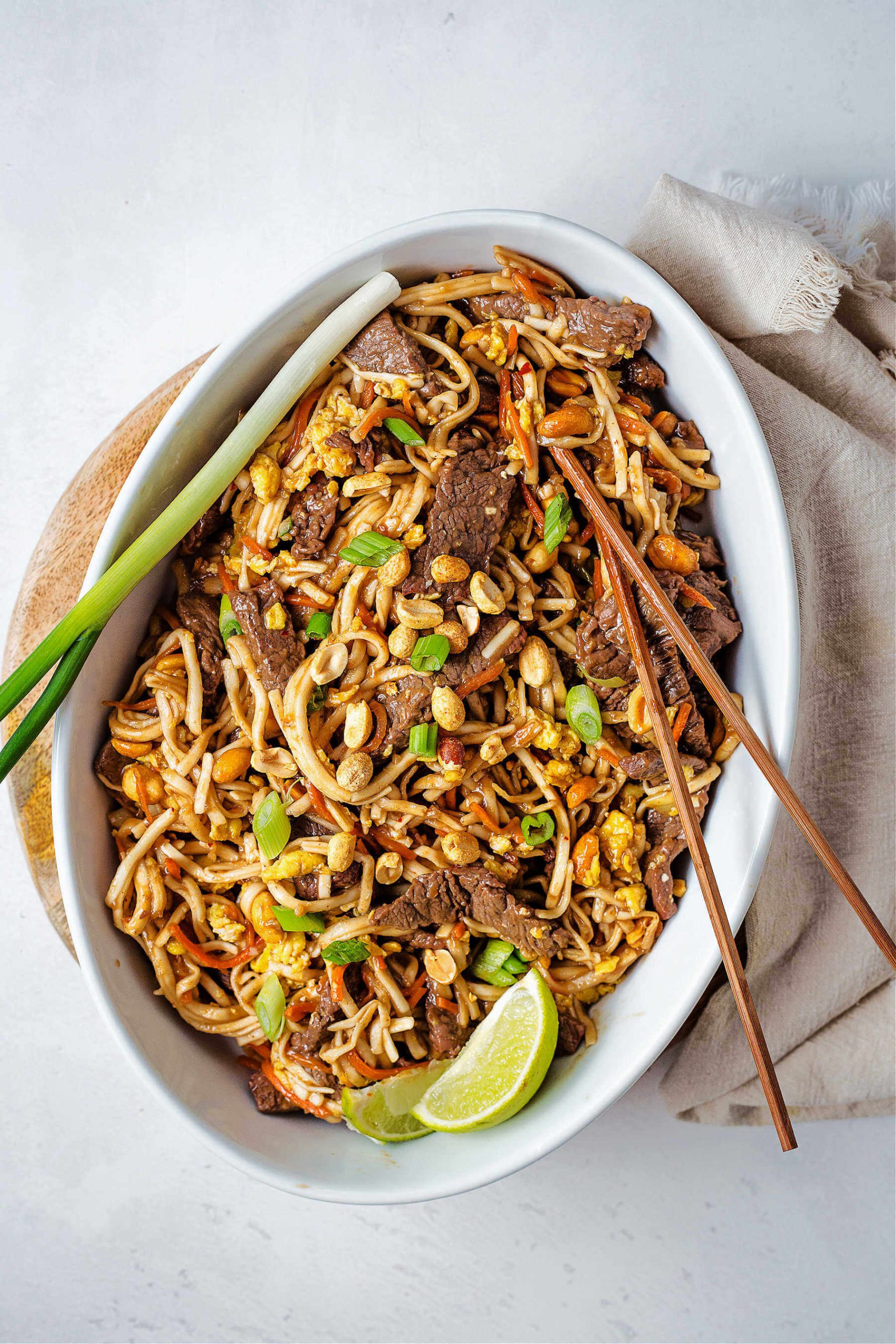 beef pad thai in a serving platter on a table and garnished with lime wedges.