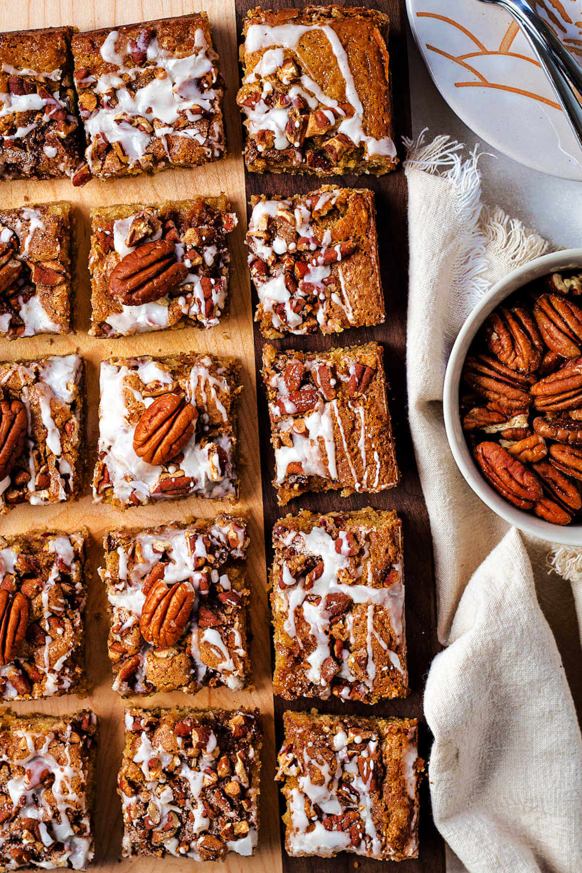 coffee cake cut into squares on a wooden board with a bowl of pecans on a table.