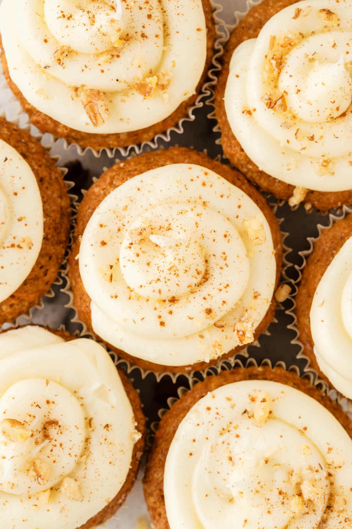 top down view of frosted carrot cake muffins with cinnamon sprinkled on top.