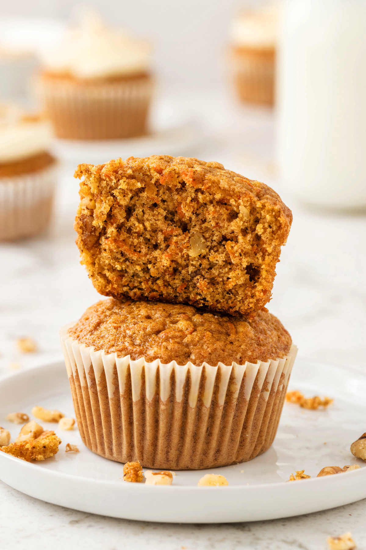 unfrosted carrot cake muffins stacked on top of each other with one cut in half to show the interior.