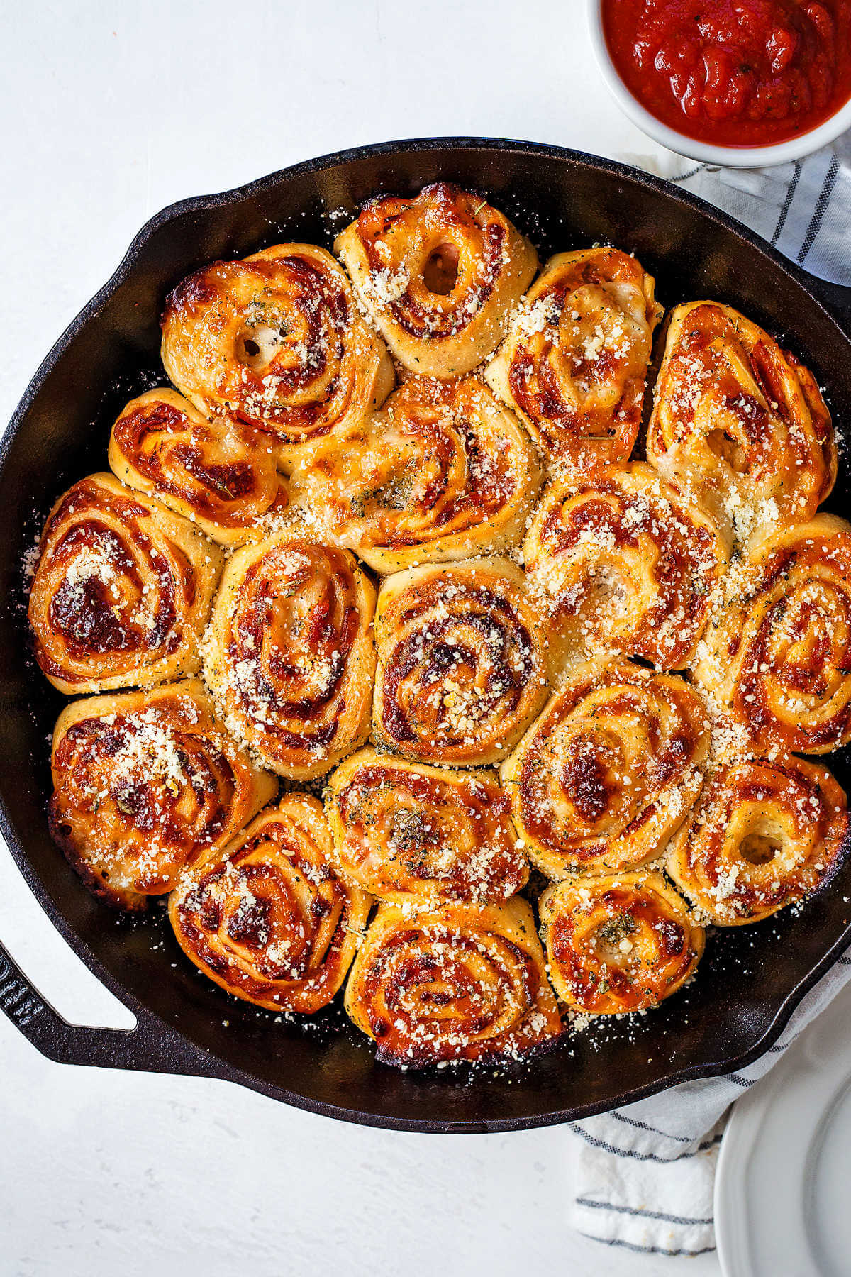 pepperoni pizza rolls in a cast iron pan on a table with a bowl of marinara.