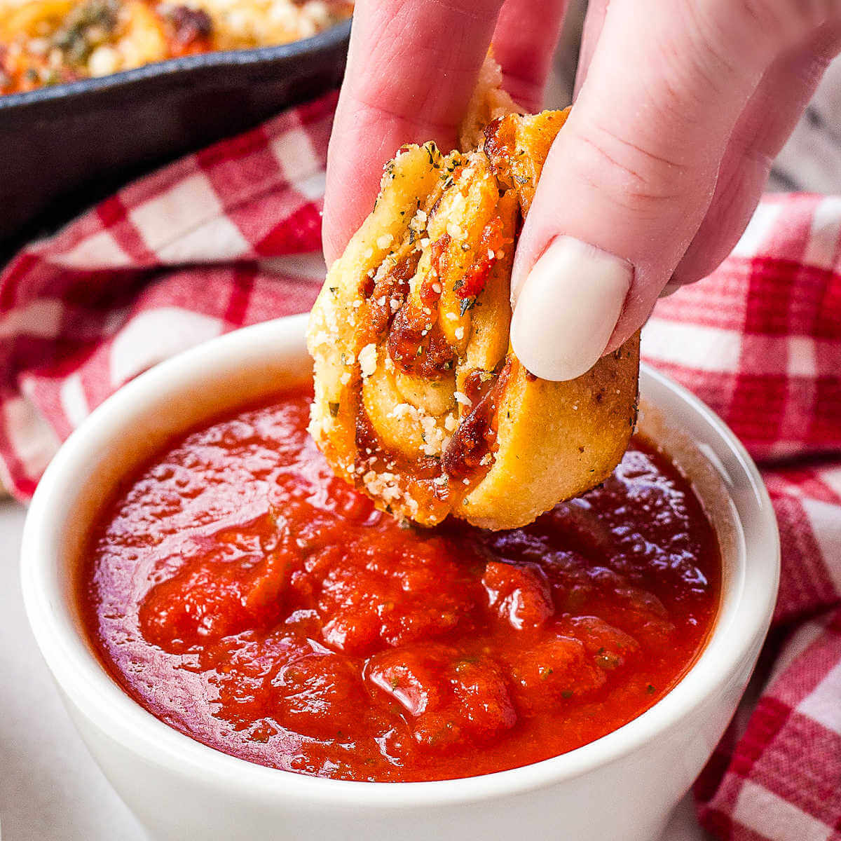 Dipping a pizza rollup into a bowl of marinara sauce on a table.