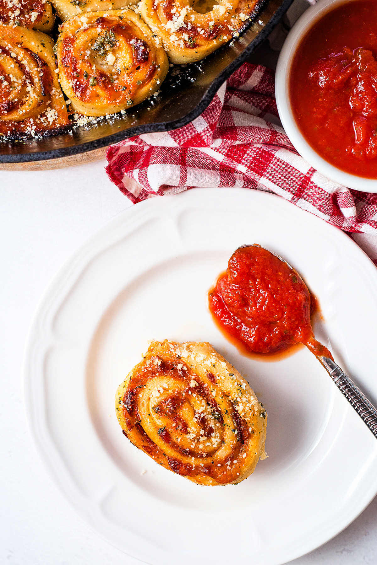 a pizza roll on a serving plate on a table with a bowl of marinara in the background.