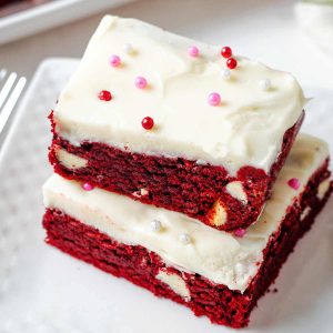 two red velvet brownies with cream cheese frosting stacked on a plate.