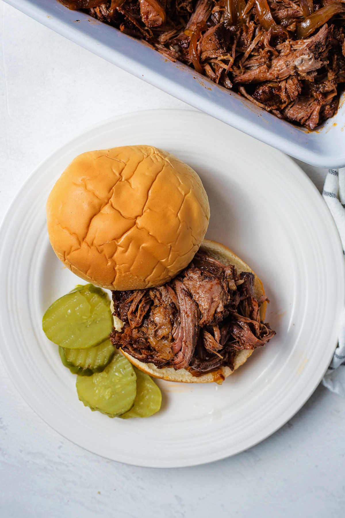 slow cooker shredded bbq beef on a hamburger bun on a plate with pickle slices.