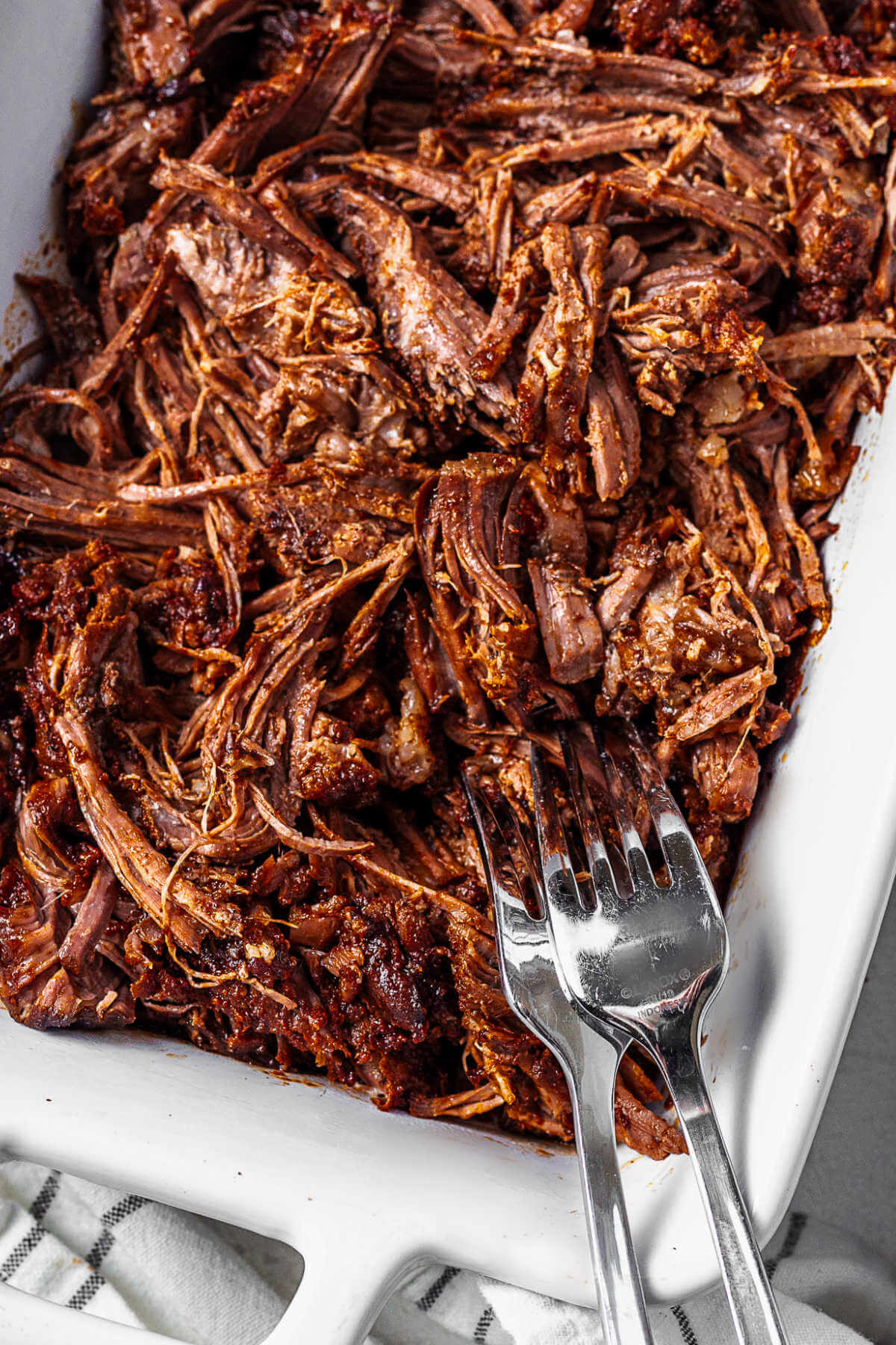 slow cooker shredded beef in a dish with two forks after shredding the roast.