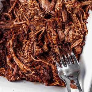 slow cooker shredded beef in a dish with two forks after shredding the roast.