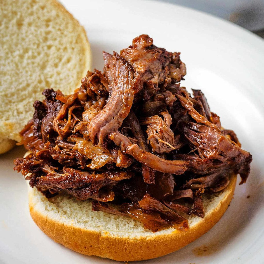pulled beef on a bun on a plate.