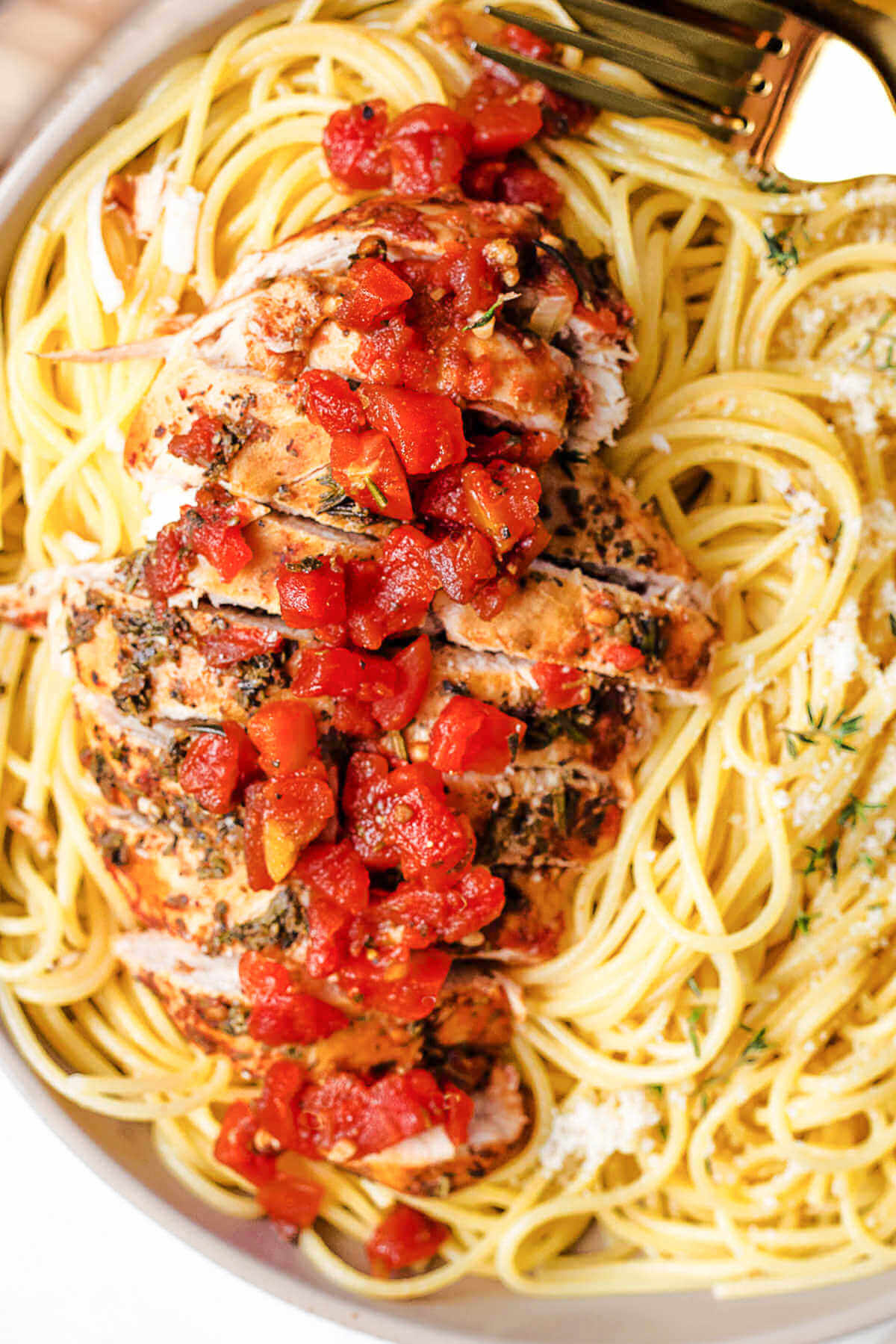 balsamic chicken sliced on top of a bed of spaghetti garnished with grated parmesan cheese.