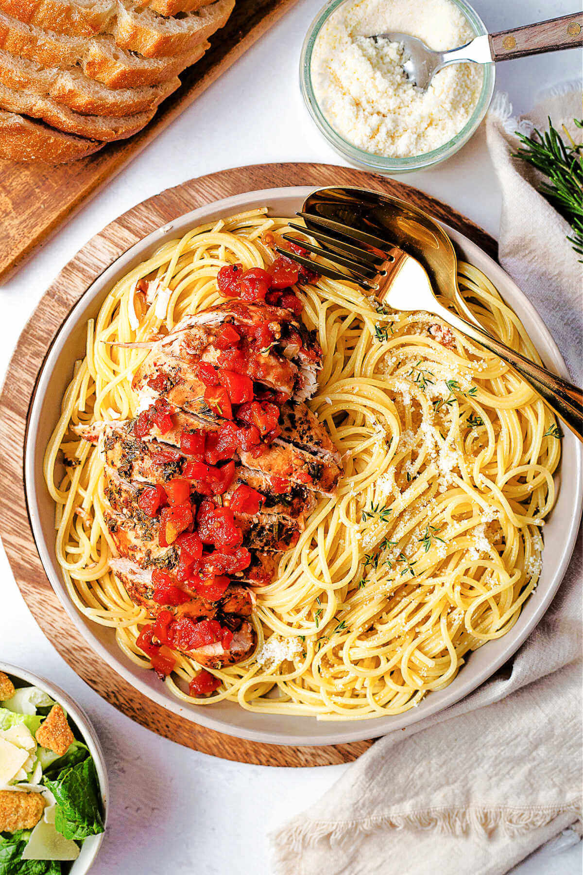 balsamic chicken sliced on top of a bed of spaghetti on a table with bread and grated parmesan cheese.