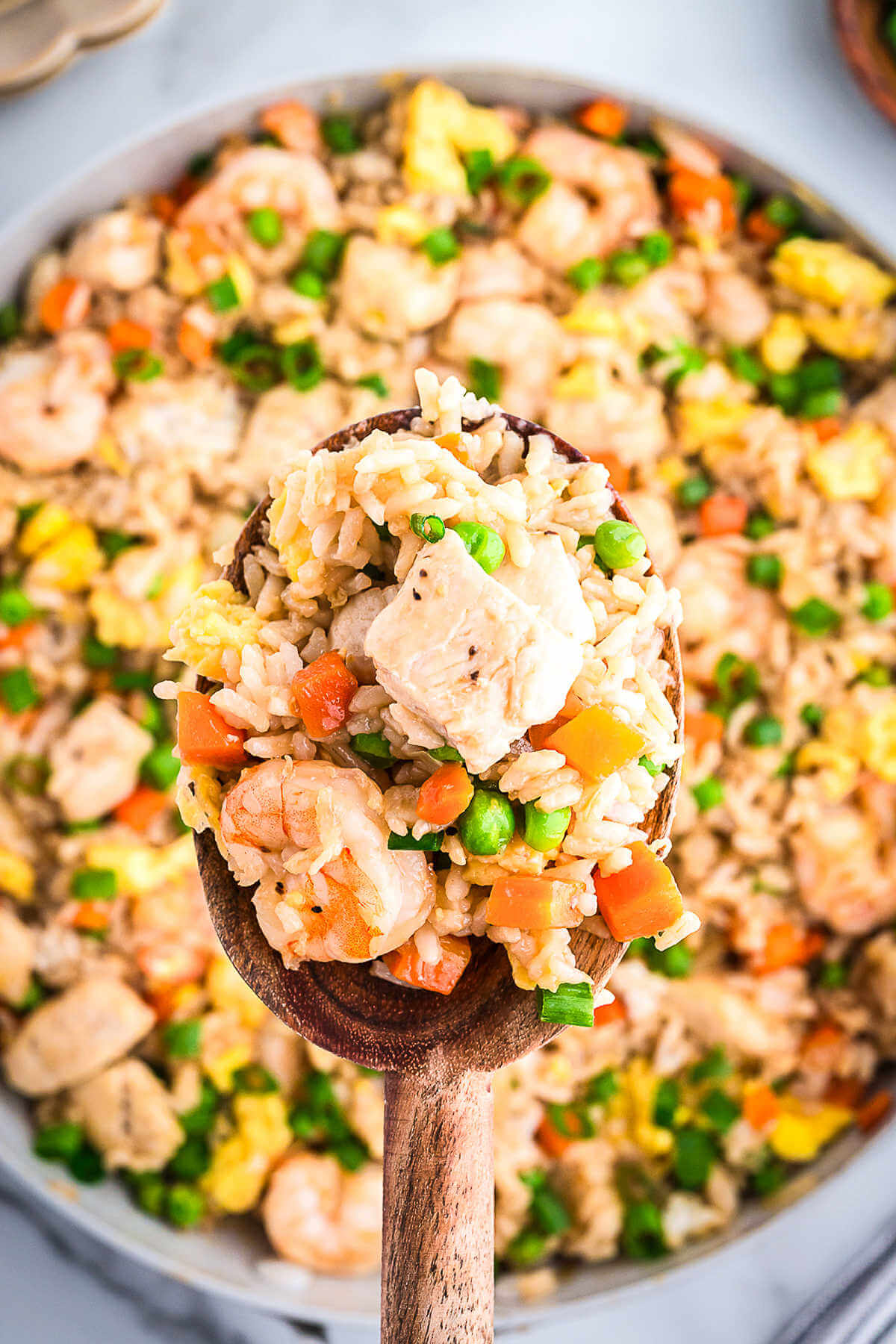 a wooden spoon lifting out a serving of shrimp and chicken fried rice from a skillet.
