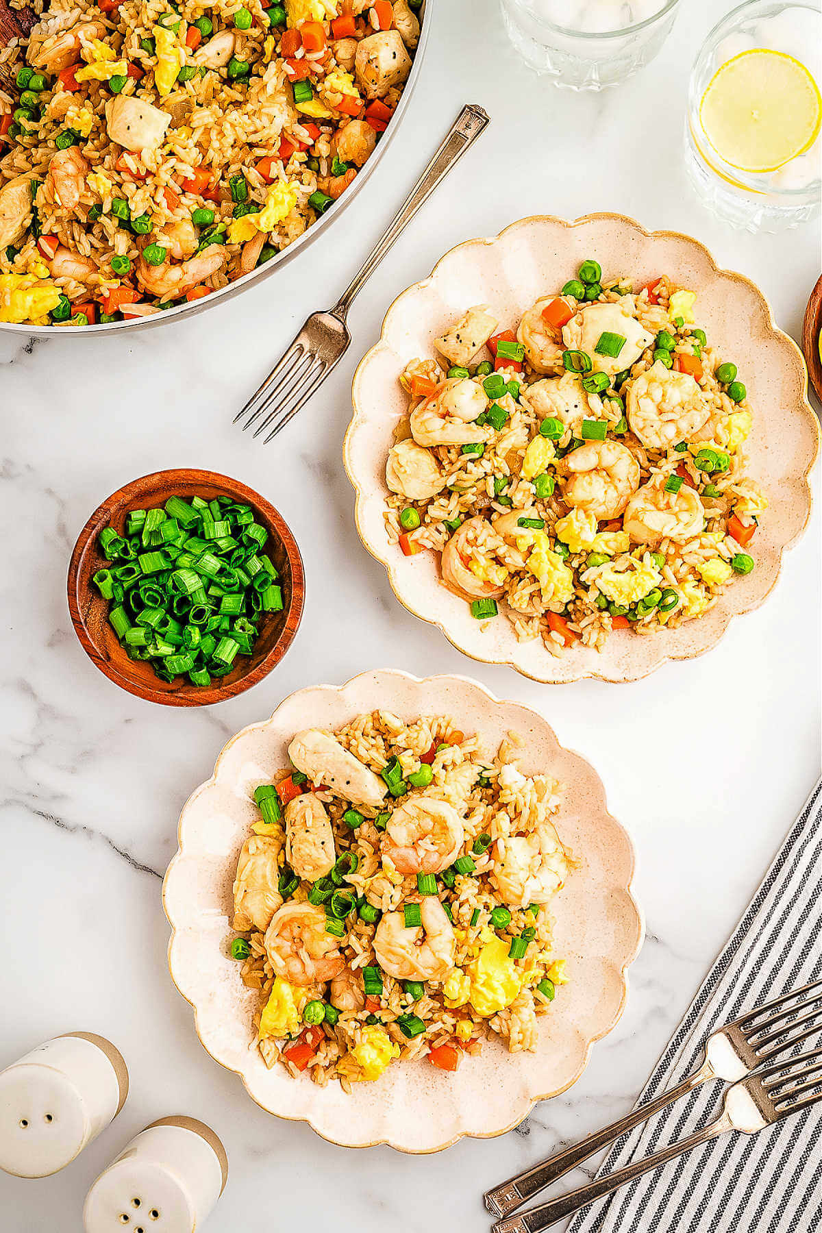 two serving plates with shrimp and chicken fried rice on a table with a bowl of sliced green onions.