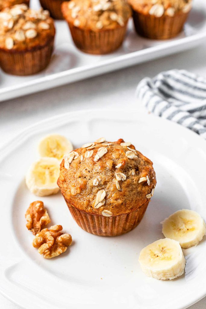 A Banana Oatmeal Muffin on a serving plate with banana slices and walnuts.
